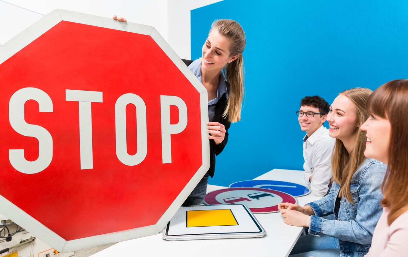 A woman holding up a stop sign and learner drivers sitting in front of her